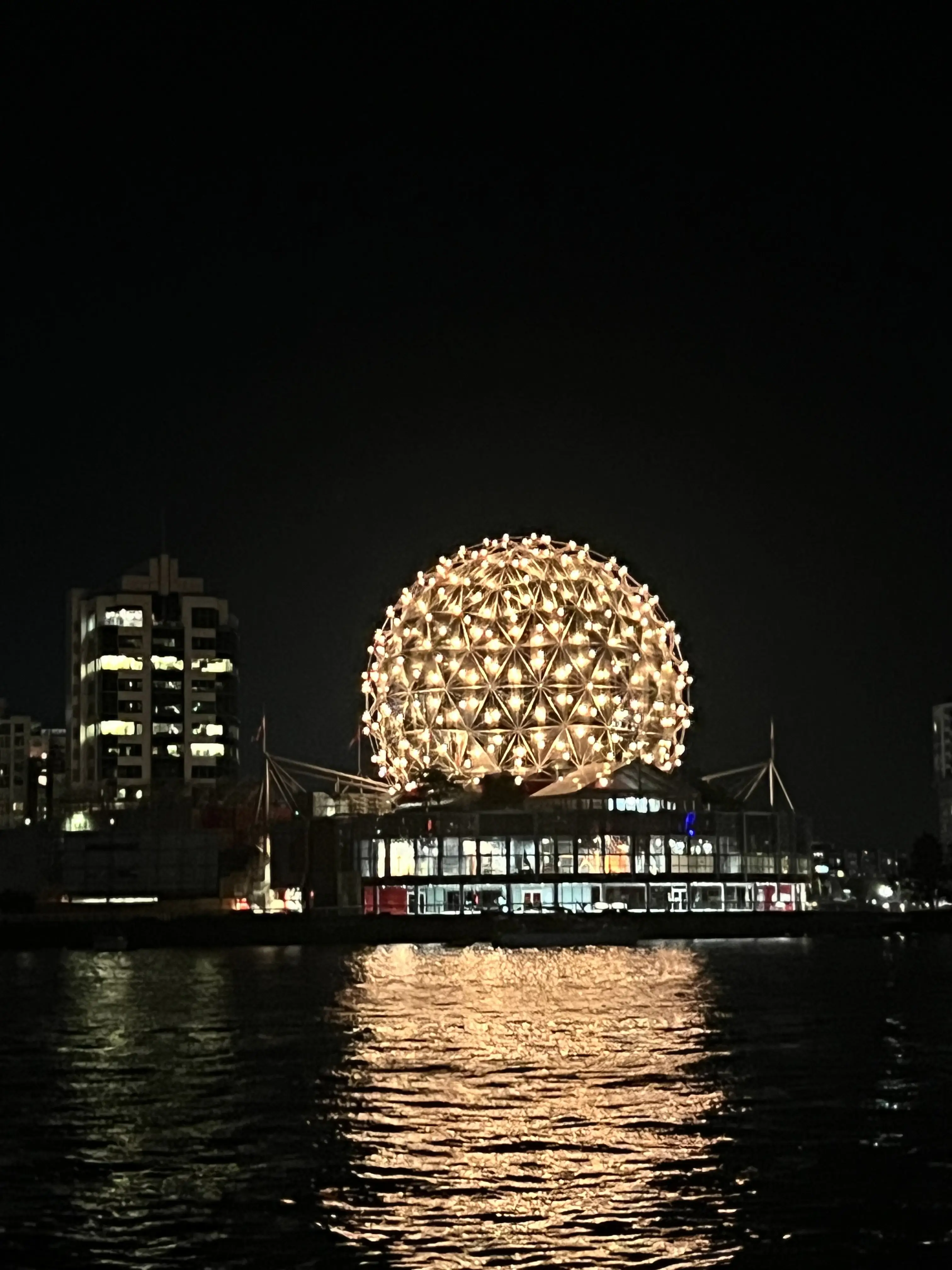 Science World lit up and reflected on False Creek at night